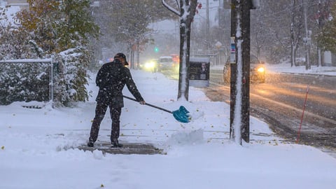 A man shovelling fresh snow from a sidewalk during an early winter storm in Toronto.