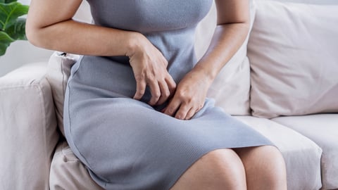 white woman in grey sleeveless dress scratching groin area