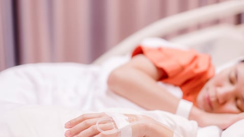 Young person laying in hospital bed with an IV in their hand
