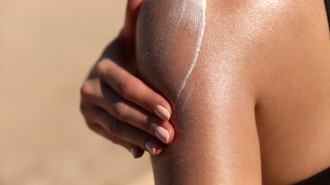 woman's bare shoulder with hand putting on sunscreen