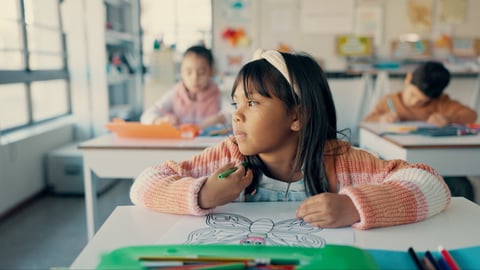 Little East Asian girl atdesk in school, distracted looking out window