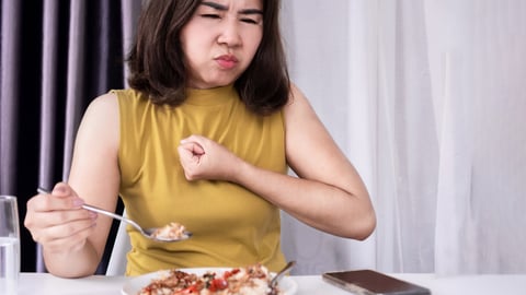 Young woman hitting her chest with a closed fist because she is choking on a bite a of food