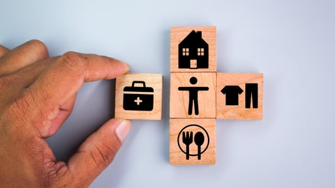 Four wooden tiles, including that of a house, a medical bag, clothes, and cutlery, surround a tile of a man