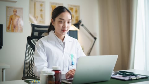 Young East Asian woman physician sitting in her office at her computer
