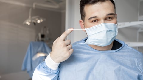 A male surgeon leaving the OR taking off his mask