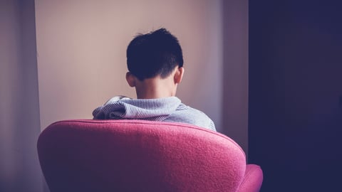 Back of a chair with a tween boy sitting, looking sad
