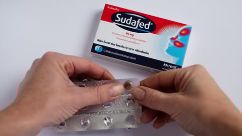 A pair of hands open a box of Sudafed, a prescription medication that contains pseudoephedrine