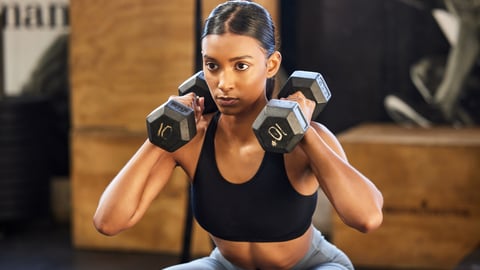 Young dark-skinned woman lifting weights while squatting in the gym