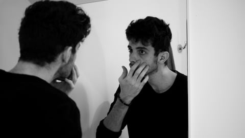 Young man examining his face pensively in a mirror