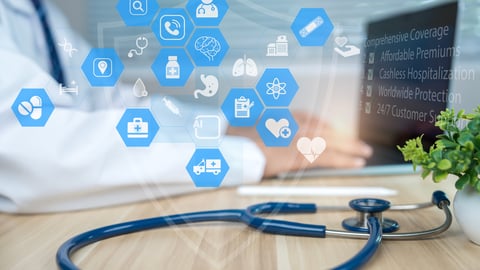 Stethoscope in the foreground while a doctor works on a laptop