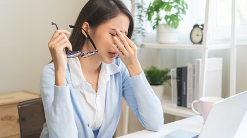 Young Asian woman holding her eyes because they hurt from looking too long at her computer