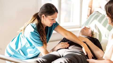 Young nurse helping an older patient turn over in bed to avoid sores