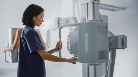 Technician facilitating a woman in the background getting a mamogram