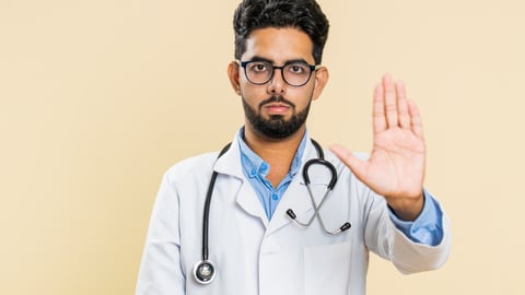 A doctor of South Asian descent holds his hand up in a stop mention, warning against something