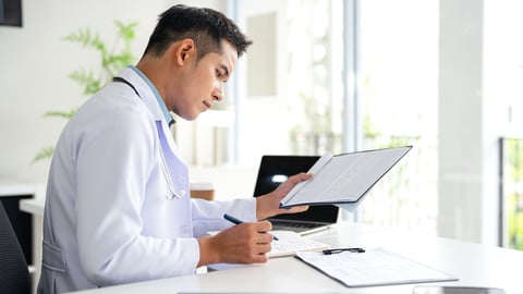 A doctor takes notes at his desk.