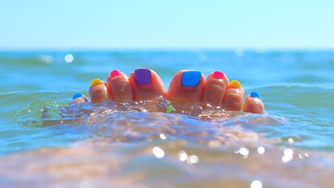 A woman's toes, painted many different colours, sticking out of the ocean