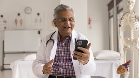 Older South Asian male doctor chatting happily on a video call with a patient