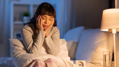 Young woman sitting on the side of the bed, suffering from insomnia