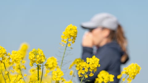 Woman sneezing from allergies with yellow flowers in the foreground