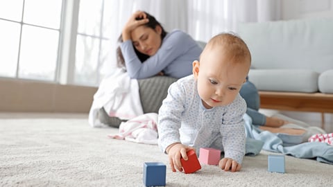 New mother struggling with her mental health as her baby plays in the foreground
