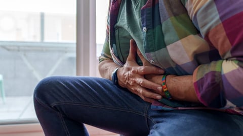 Older man in a colourful shirt holding his stomach in pain