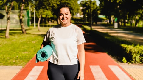 Young plus size woman carrying a yoga mat outside 