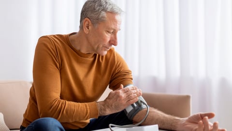 Older white man in an orange shirt taking his blood pressure at home