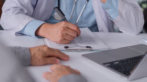A family doctor writes a prescription on a clipboard document during medical consultation