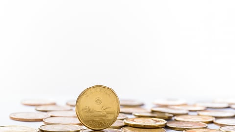 A loonie stands on its edge, next to a pile of other loonies