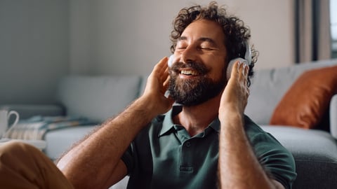 A man listens to music with headphones, smiling.