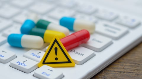 An exclamation mark sign and a pile of pills on a computer keyboard, representing the potential hazards of online drug information.