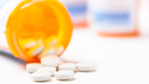 Round white prescription medication medicine pill tablets spilling from a bottle with numerous full bottles in background