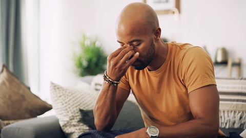 Young Black man in orange t-shirt holding his forehead because of sinus pain