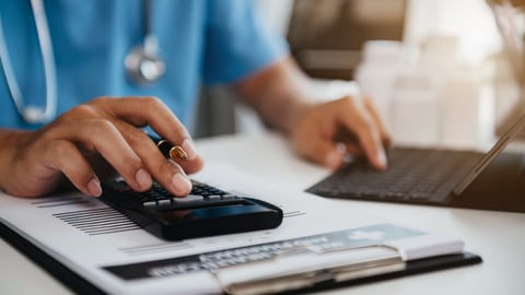 A doctor holding a calculator while on the computer.