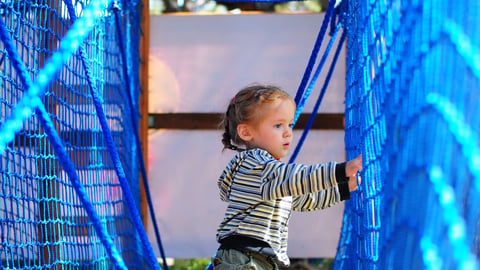 A young toddler playing in a rope obstacle course