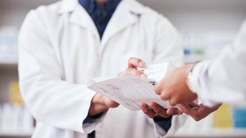 Closeup of pharmacist exchanging medication and a prescription.