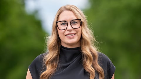 A blonde woman with glasses standing outside