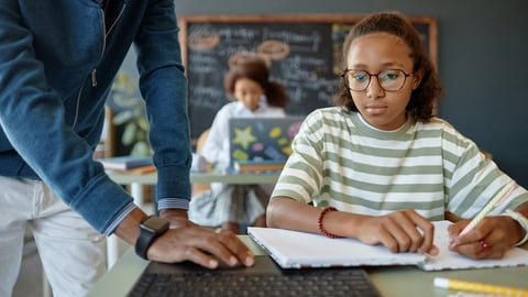 Young Black girl being shown something on a computer by her teacher