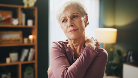 An older woman in a purple shirt holding her shoulder in discomfort