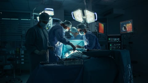 A team of doctors perform surgery in a dark operating room.