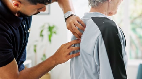 A chiropractor massages the back of an elderly man. 