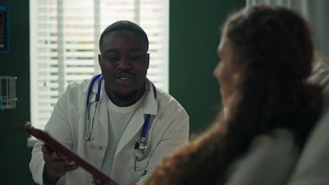 A young doctor chatting with a patient in a hospital bed, showing her a consent form on a tablet