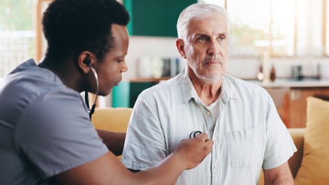 A young doctor listening to an older male patient's heart