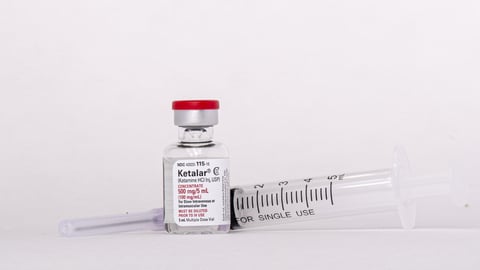 A vial of ketamine next to a syringe. 