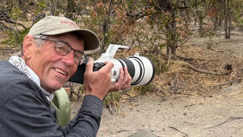 Dr. Don Gutoski holds a camera in front of wildlife.