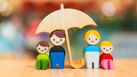 A little toy family with the father holding an umbrella over everyone