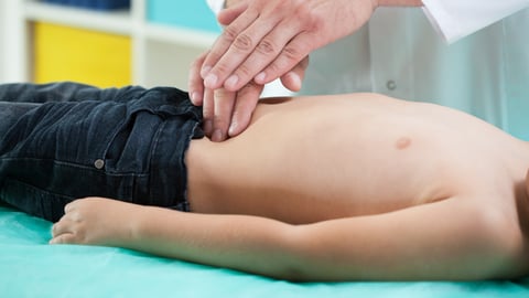 torso of boy lying down with pediatrician examining abdomen with hands.