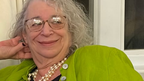 Dr. Perle Feldman in a green shirt and pearls, reclining on a sofa