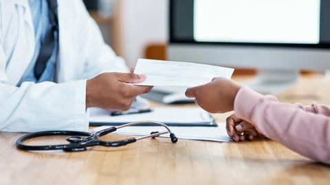 A doctor hands a patient a sick note.