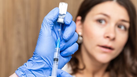 A woman looking worried as a pharmacist fills a syringe
